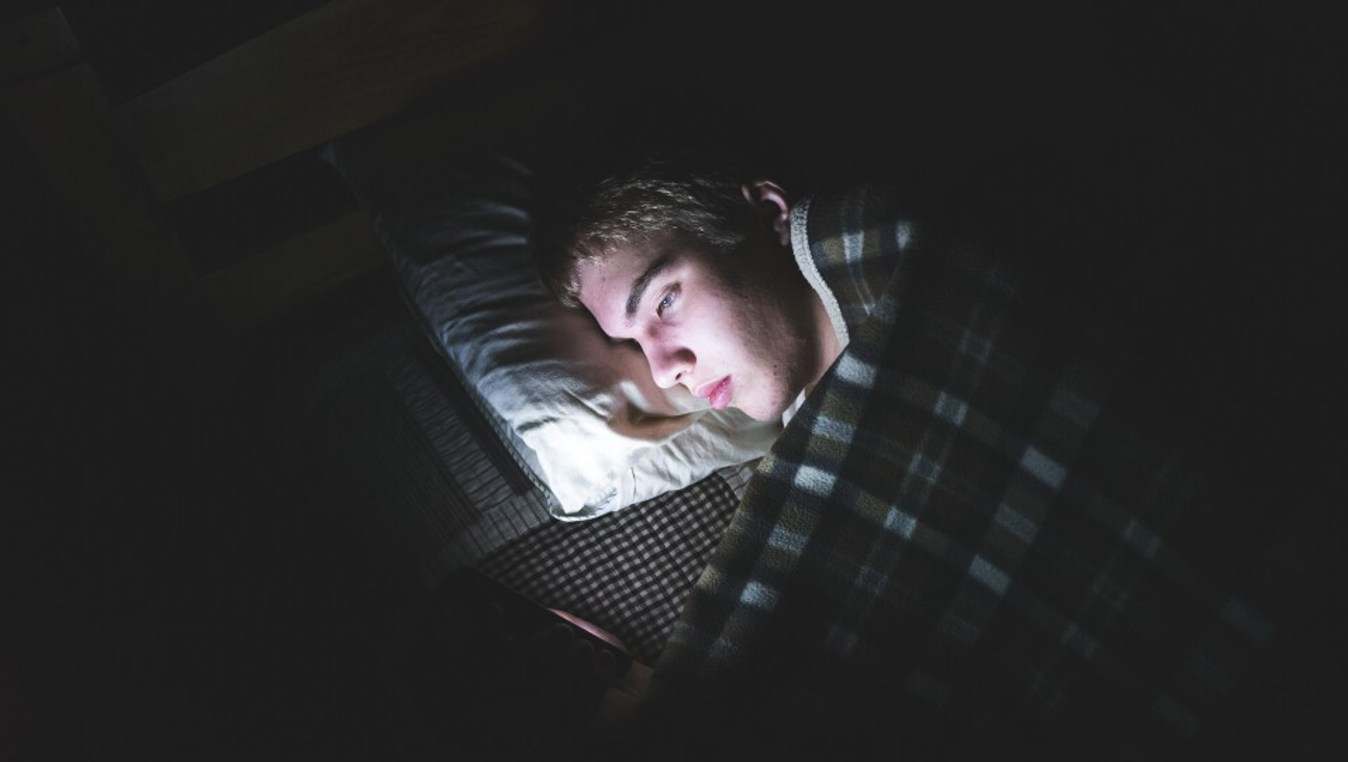 Teenage boy lying in the dark on his phone